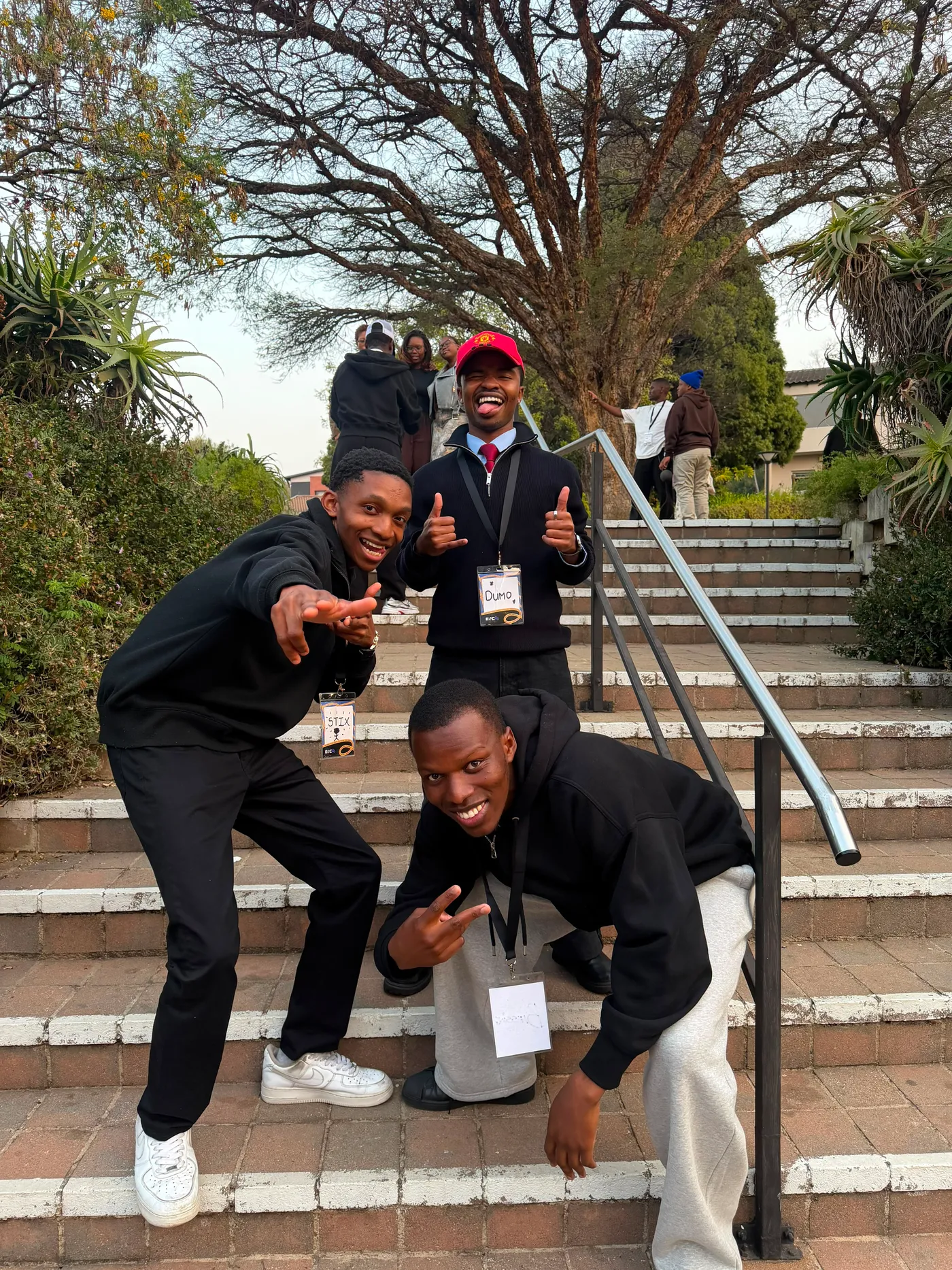Blessing crouching on brick steps with two friends, all three wearing name badges and pulling poses for the camera
