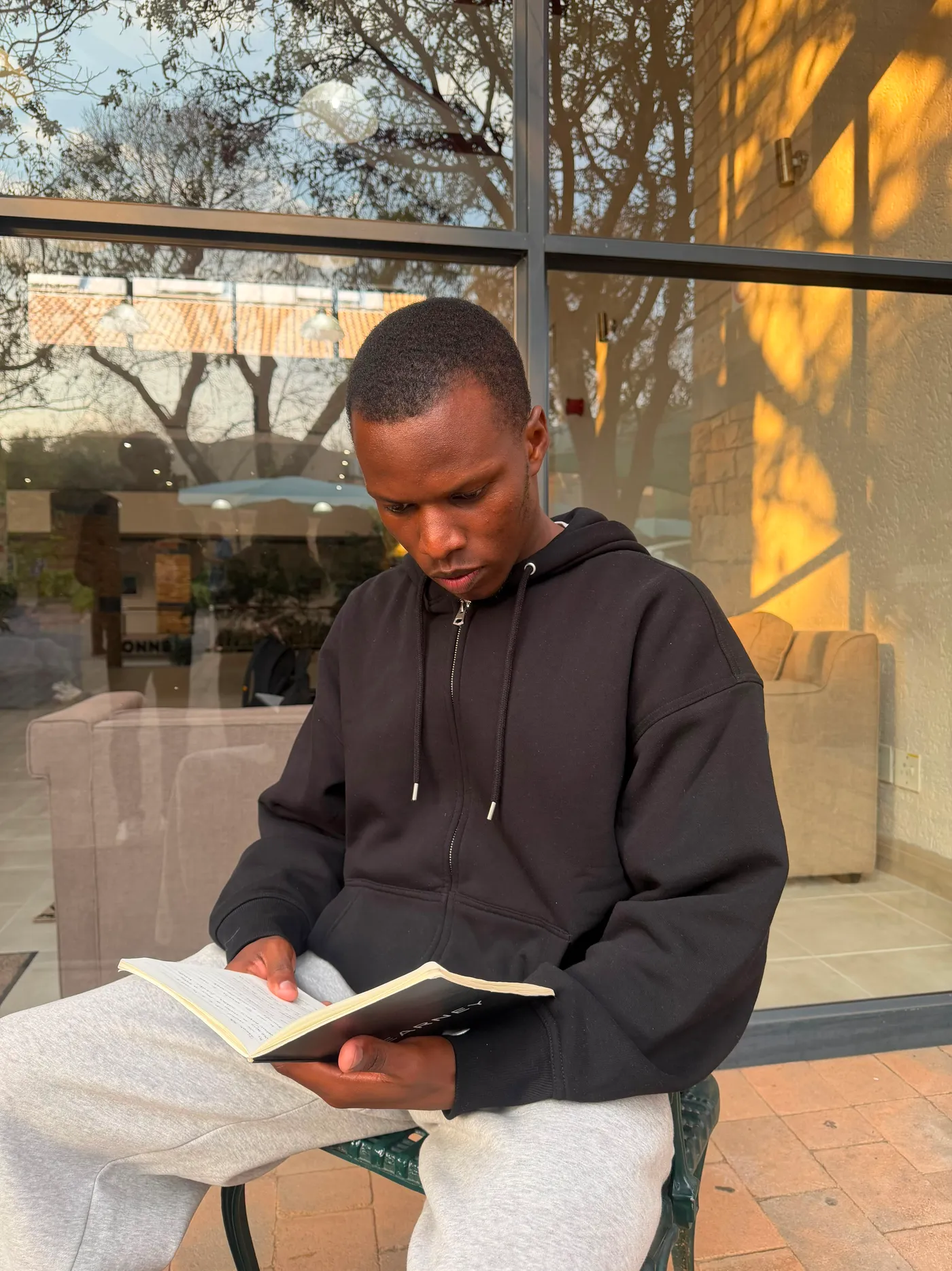 Blessing reading beside a glass frontage, bare trees reflected in the panes