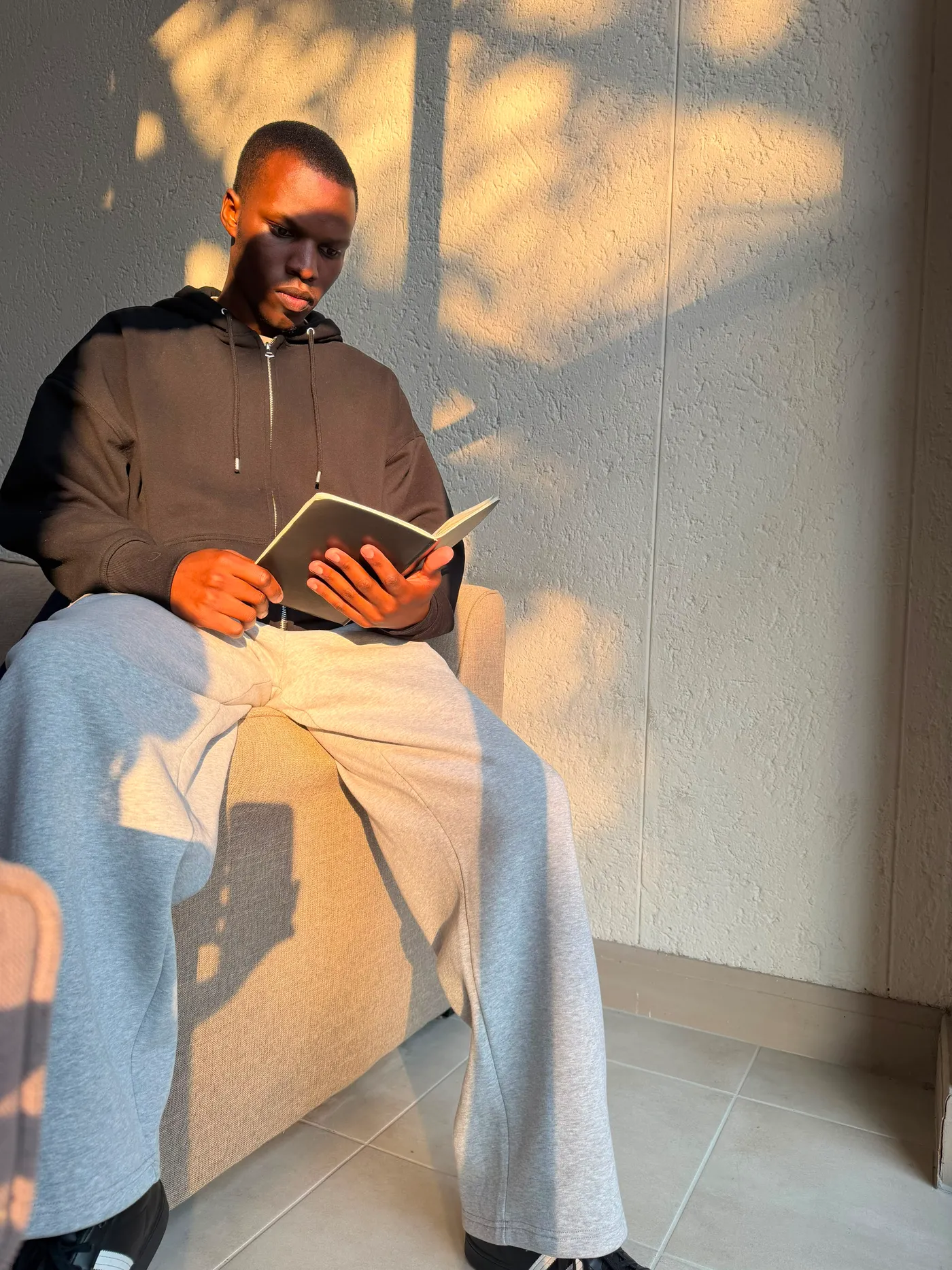 Blessing reading in a chair as leaf shadows move across the wall beside him