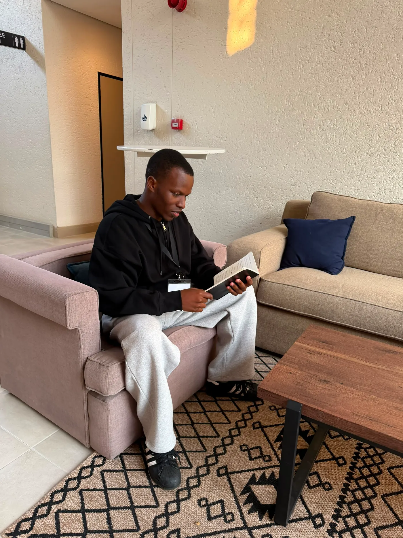 Blessing reading in a lounge, a patterned rug and low wooden table in front of him